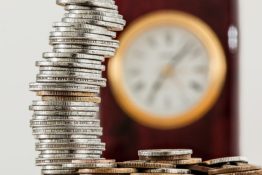 A stack of coins in front of a clock