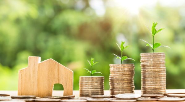 a wooden house model next to two stacks of coins with plants growing out of them