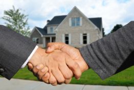 Buying a second home in 2020: two hands shaking in front of a suburban house