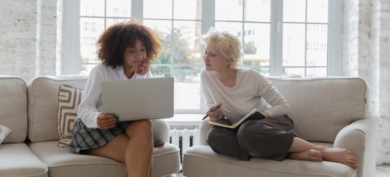 two women sitting in their living room trying to find movers on short notice on their laptop