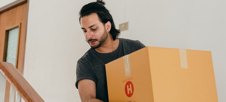 a man carrying an essentials box downstairs