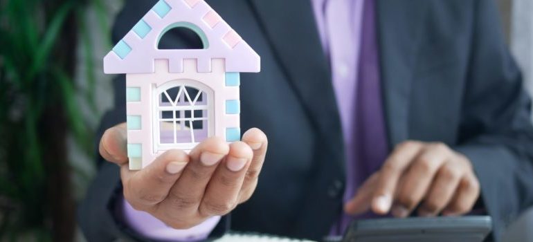 a man holding a model house, symbolizing an incentive to invest in your Brooklyn rental property