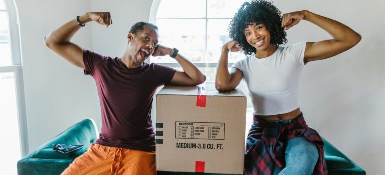 two people flexing with a moving box in between of them