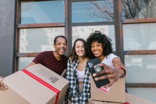 three people with a moving box taking a selfie shows the way you should help your friend move from Queens to Manhattan