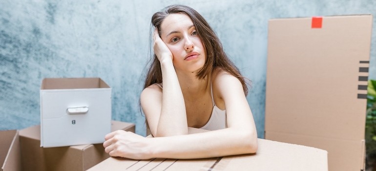 A woman surrounded by boxes thinking about leaving Chelsea after a job loss. 